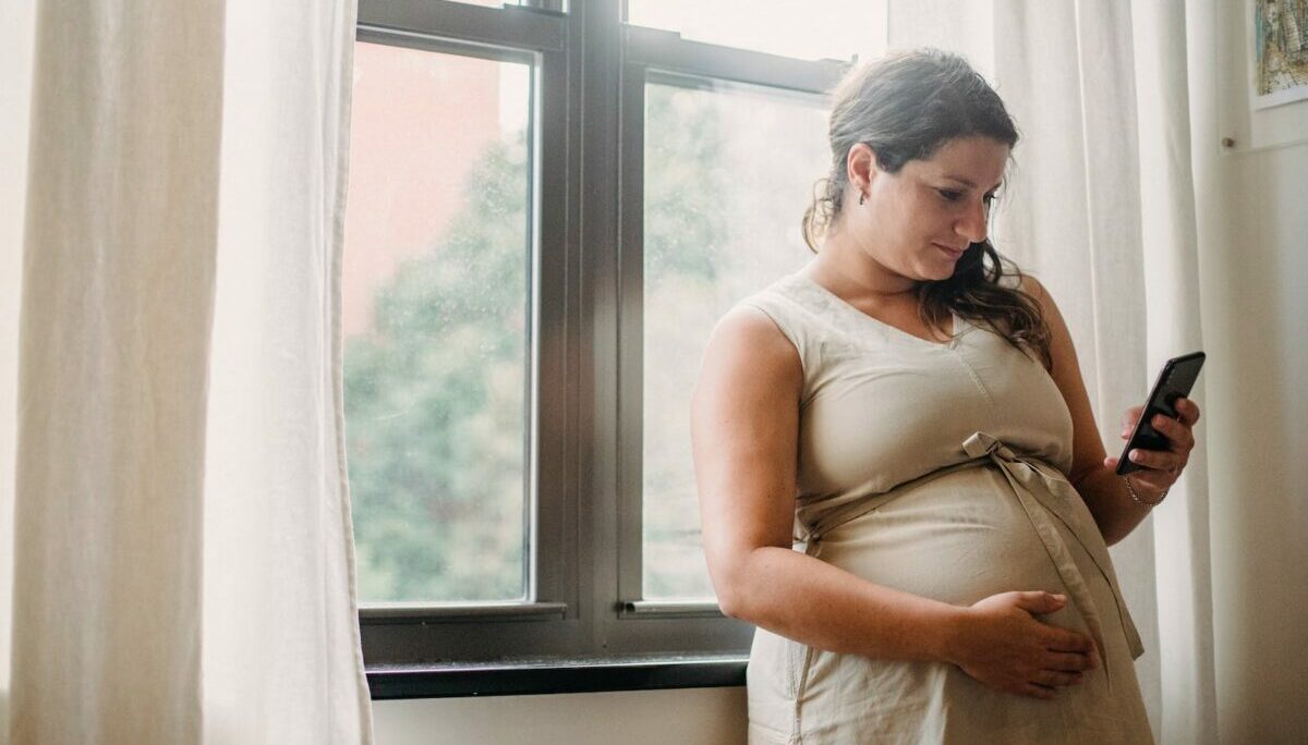 Pregnant woman using cellphone while standing at home
